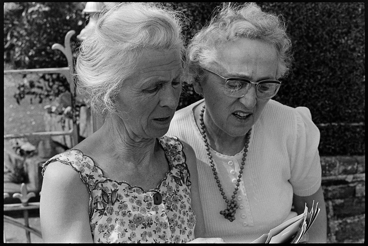 Two women, sisters. 
[Marge Knight, on the left and Dot Heard, on the right, sisters, looking at photographs outside Arscotts, Dolton.]