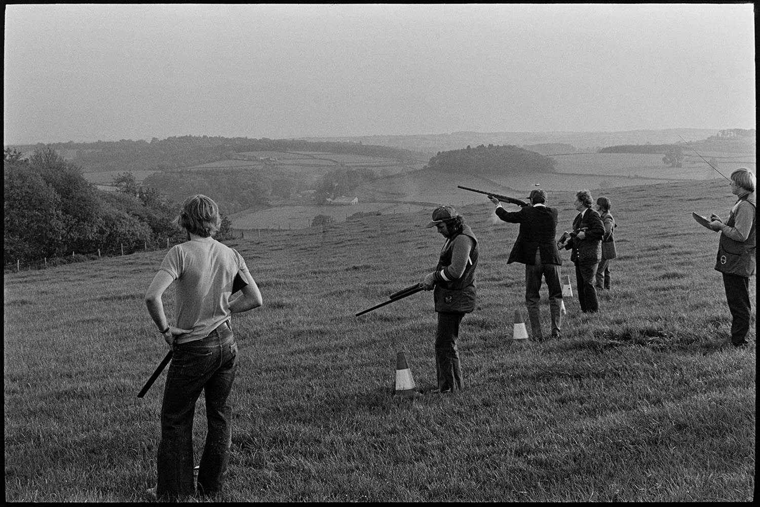 Clay pigeon shoot and games roulette for champagne. 
[Men shooting in a field at a clay pigeon shoot at Harepath, Beaford. A landscape of fields and trees is visible in the background.]
