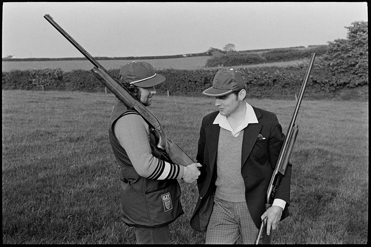 Clay pigeon shoot and games roulette for champagne. 
[Two men holding shotguns and wearing caps at a clay pigeon shoot at Harepath, Beaford.]