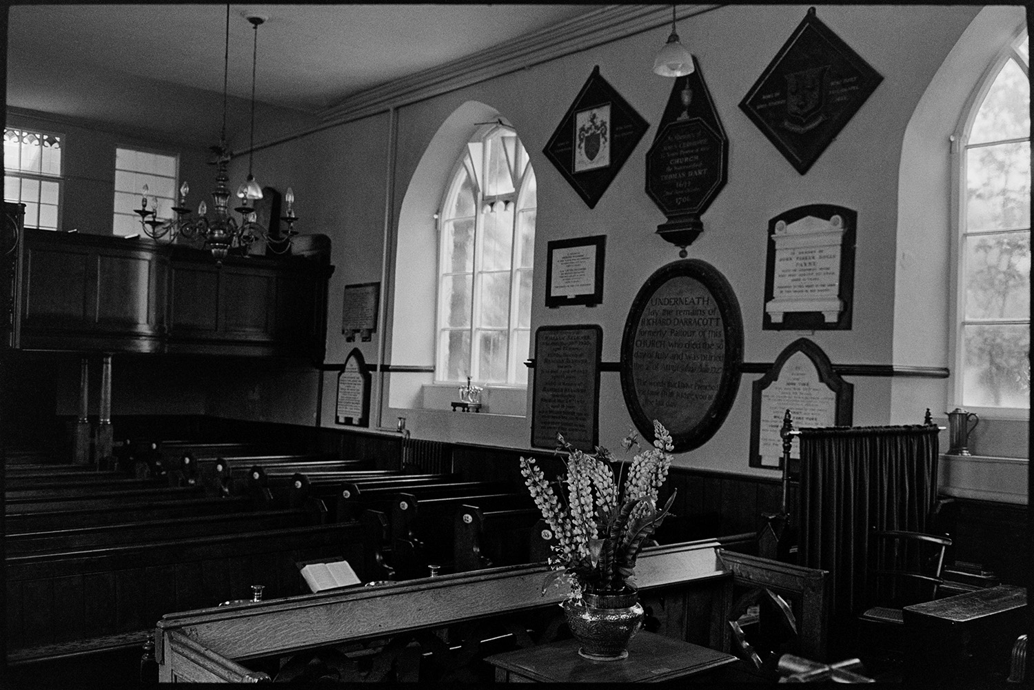 Interior and exterior of old Congregational chapel, wall plaques, stairs and railings. 
[The interior of the Congregational Chapel in East Street, Chulmleigh. Pews, a balcony, a flower arrangement and wall plaques are visible.]