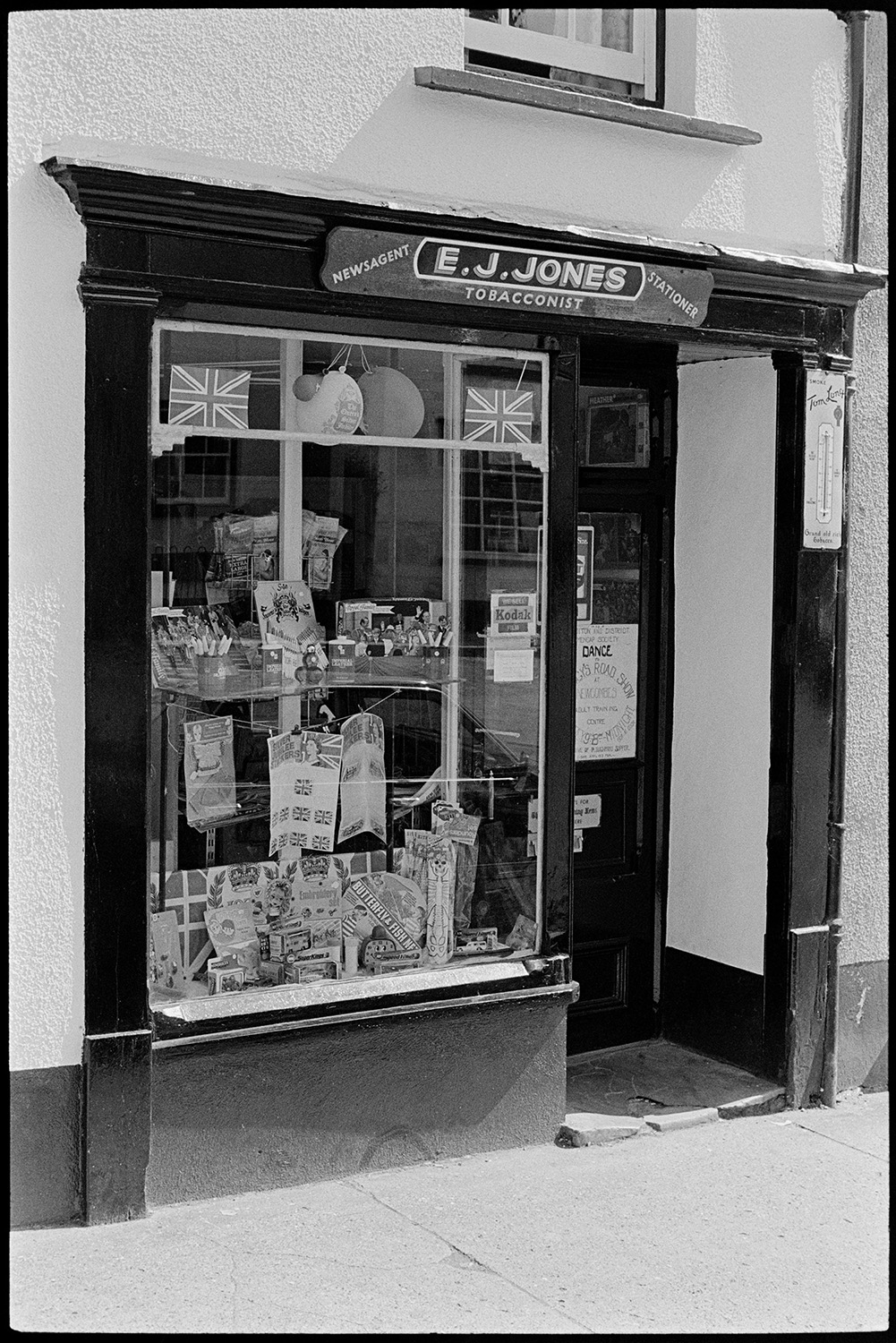Newsagent and tobacconists shop. 
[The shop front window of E J Jones, Tobacconist, Newsagent and Stationer in Winkleigh. The window is decorated with Union Jack flags, balloons and royal memorabilia to celebrate the Silver Jubilee of Queen Elizabeth II.]