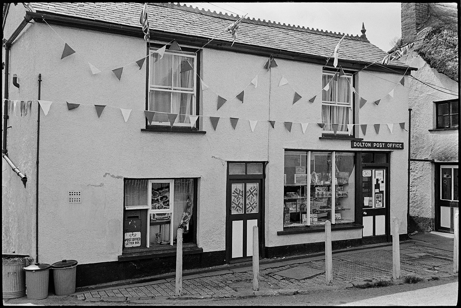 Front of Post Office with flags for Jubilee. 
[The front of Dolton Post Office in Fore Street, Dolton. The building is decorated with Union Jack flags and bunting to celebrate the Silver Jubilee of Queen Elizabeth II.]
