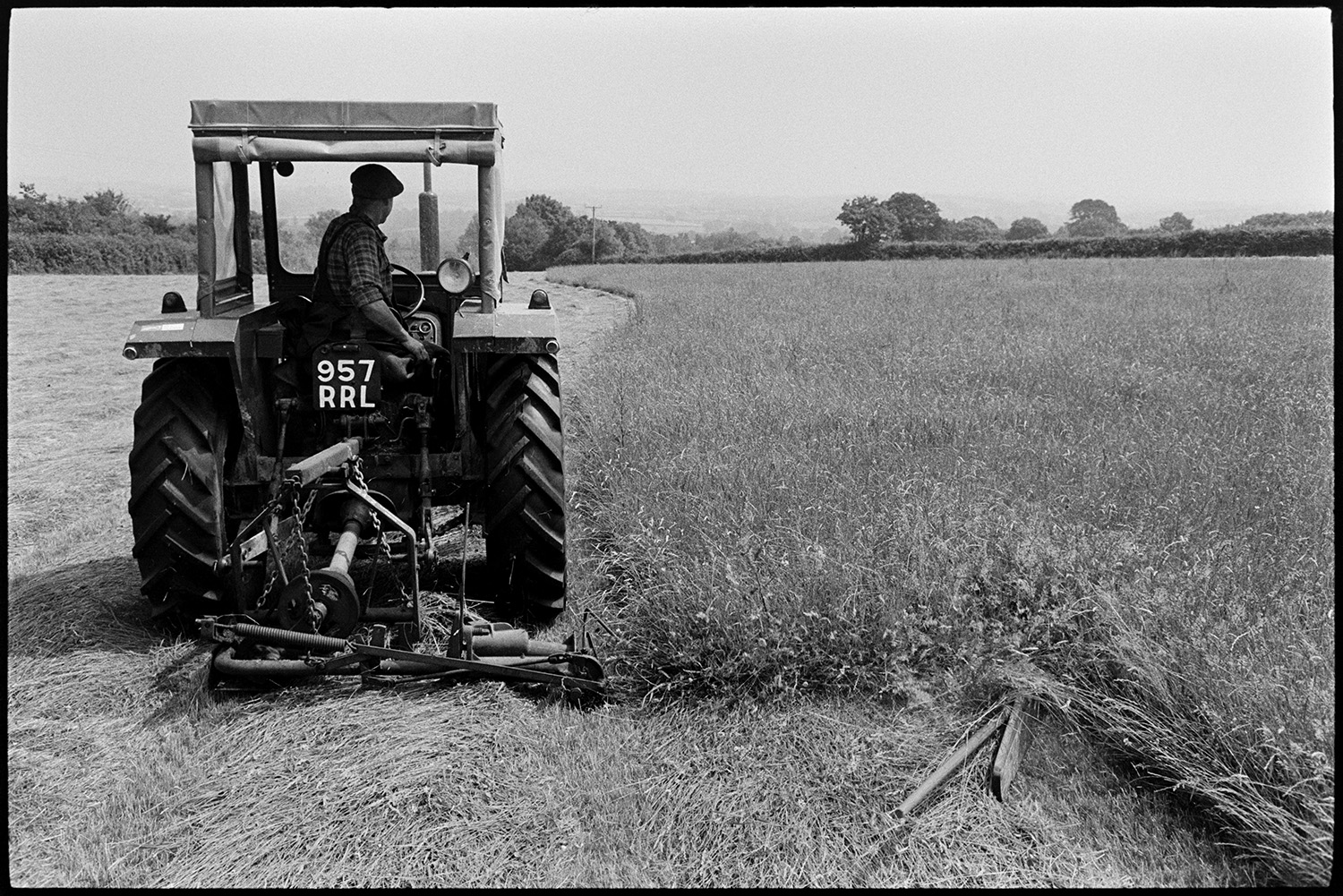 Farmer cutting grass, hay with tractor and cutter. 
[Mr Oke using a mower and tractor to cut grass in a field at Deckport, Hatherleigh for hay.]