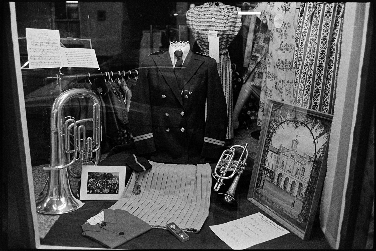 Shop window decorated for fair. 
[A shop window decorated with two brass musical instruments, a band member jacket, pictures and clothes in South Molton for the South Molton Fair.]