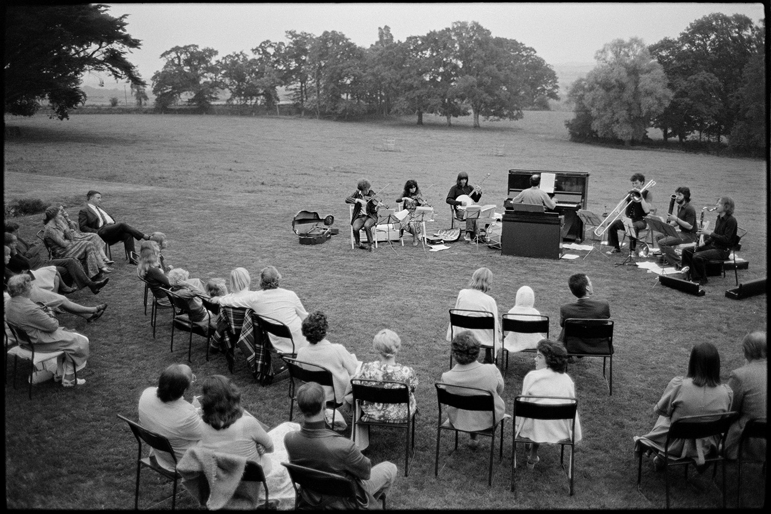 Open air concert, Beaford Event. 
[Spectators sat on chairs in a field at Nethercott, Iddesleigh listening to an open air concert by Michael Nyman and his band. The event was organised by The Beaford Centre.]