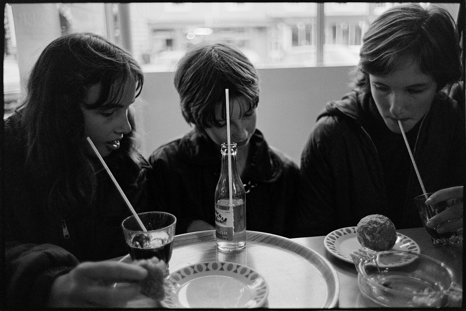 Three teenagers in a café eating doughnuts and drinking  drinks with straws.