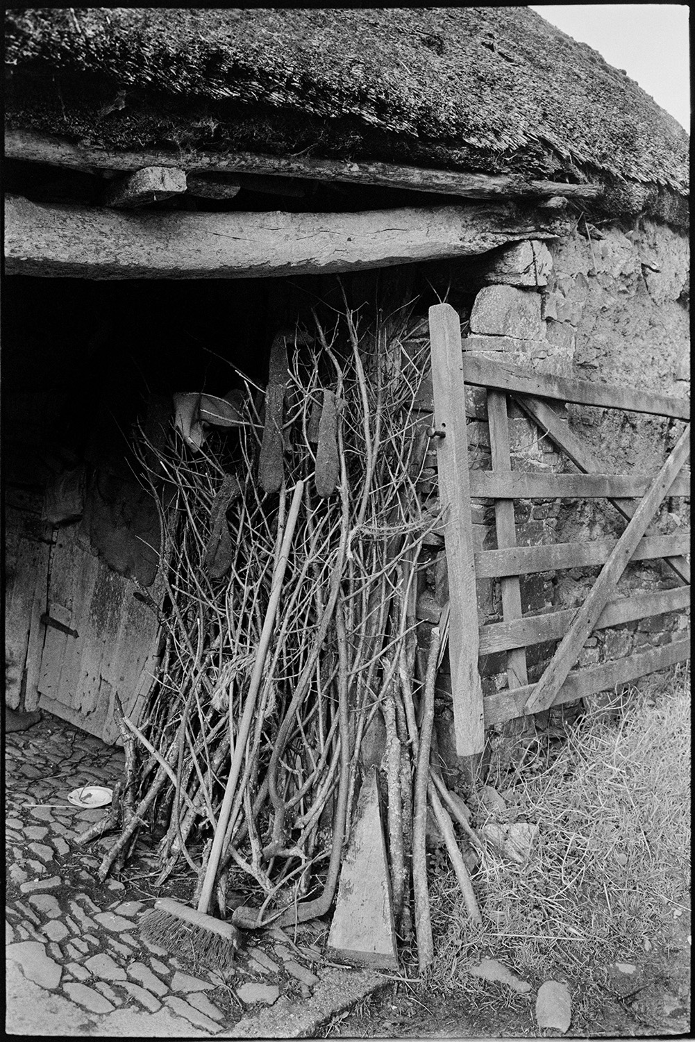 Socks hanging to dry on stack of kindling in barn. 
[Socks hung on kindling to dry in a thatched barn at Bridgetown, Iddesleigh. A brush is also lent against the branches, and a field gate is propped against the barn wall.]