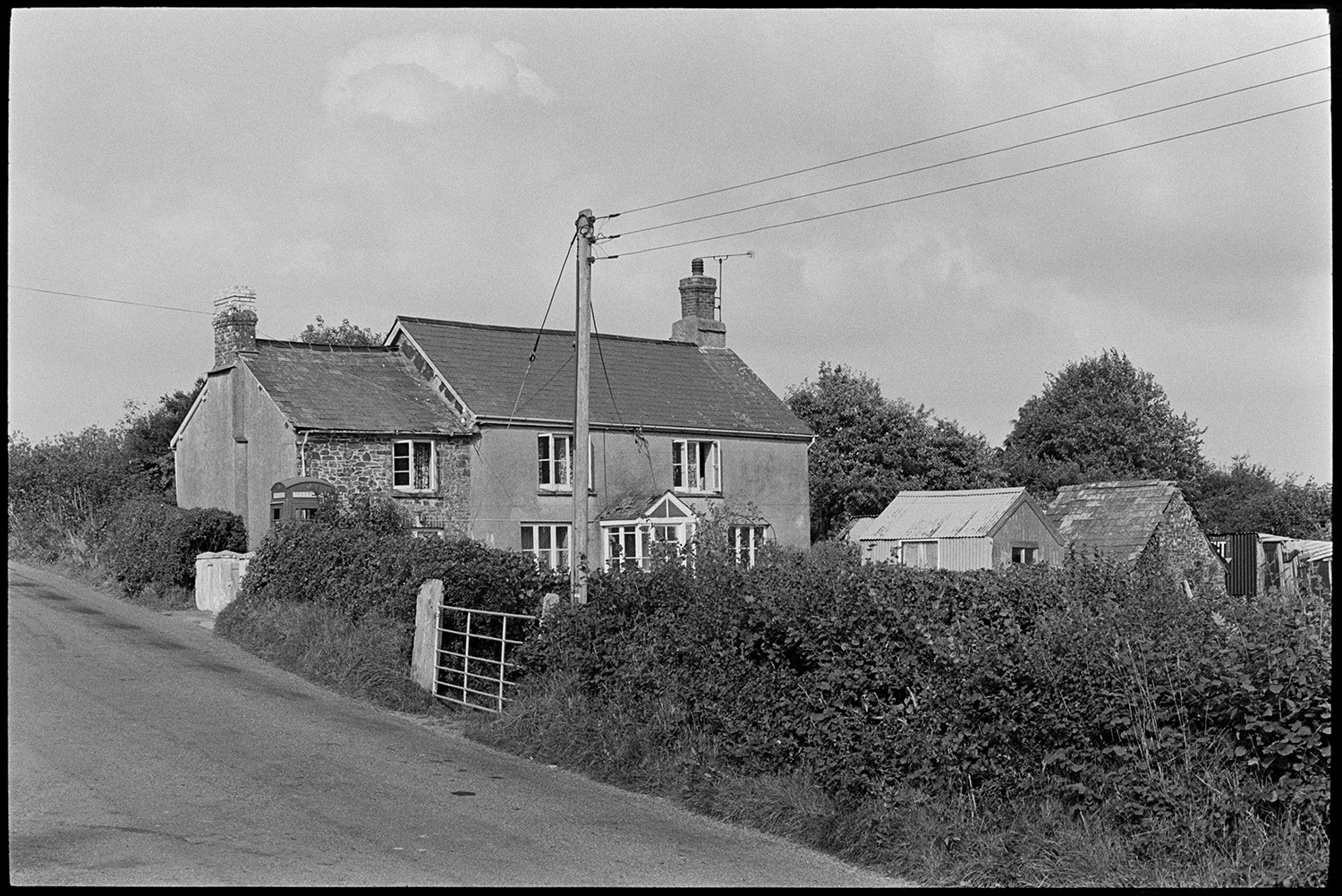 Houses taken to compare with photos in the old Archive by George Tucker. 
[A house in Peters Marland, Burrington with a telephone box outside. Various sheds and barns are visible behind a field gate.]