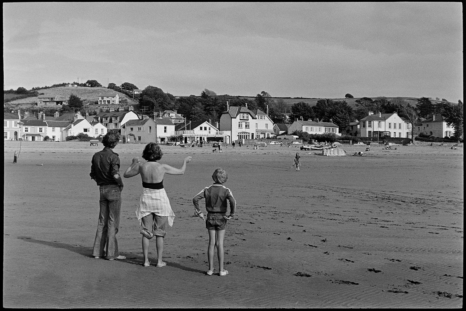 Children playing on beach, kite. Abandoned barge. 
[Holidaymakers on the beach at Instow. A family are trying to fly a kite. The buildings on the seafront are visible in the background.]
