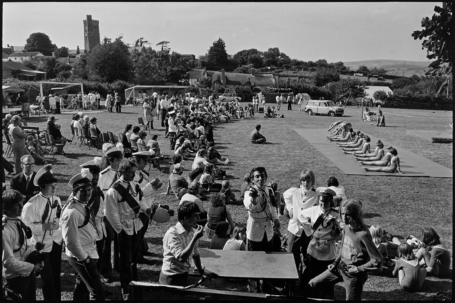 Gymnasts at fete. 
[Gymnasts performing at Atherington Village fete. A crowd is watching them. In the foreground bandsmen can be seen playing a game of darts.]