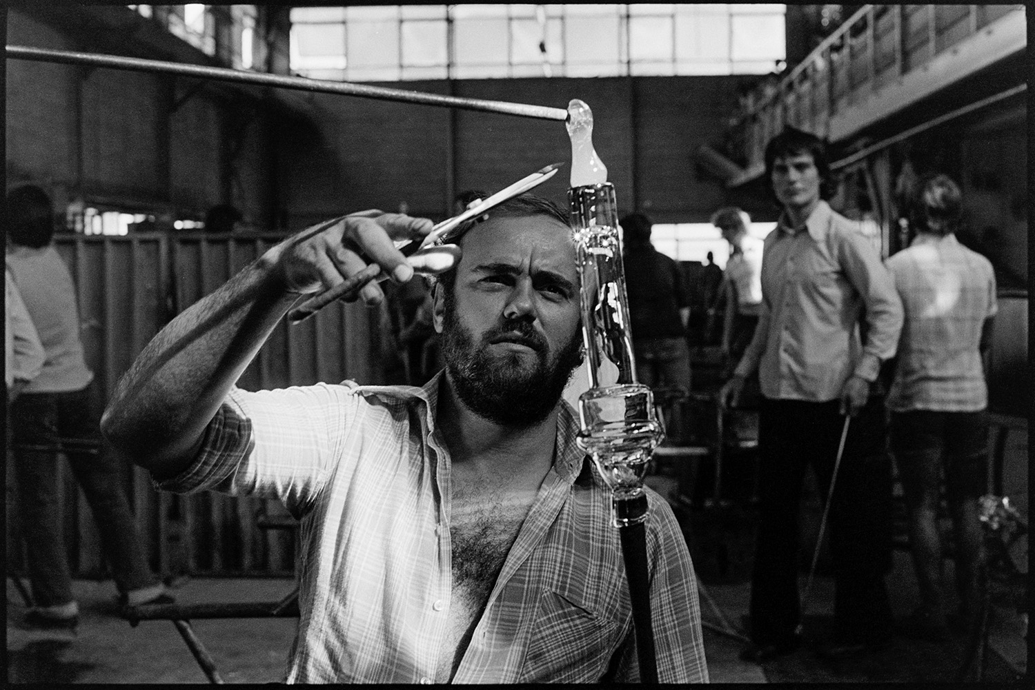 Management and workers at glass factory. 
[A man about to cut a piece of molten glass at the Dartington Glass factory, now known as Dartington Crystal, in Torrington. Other workers can be seen in the background.]