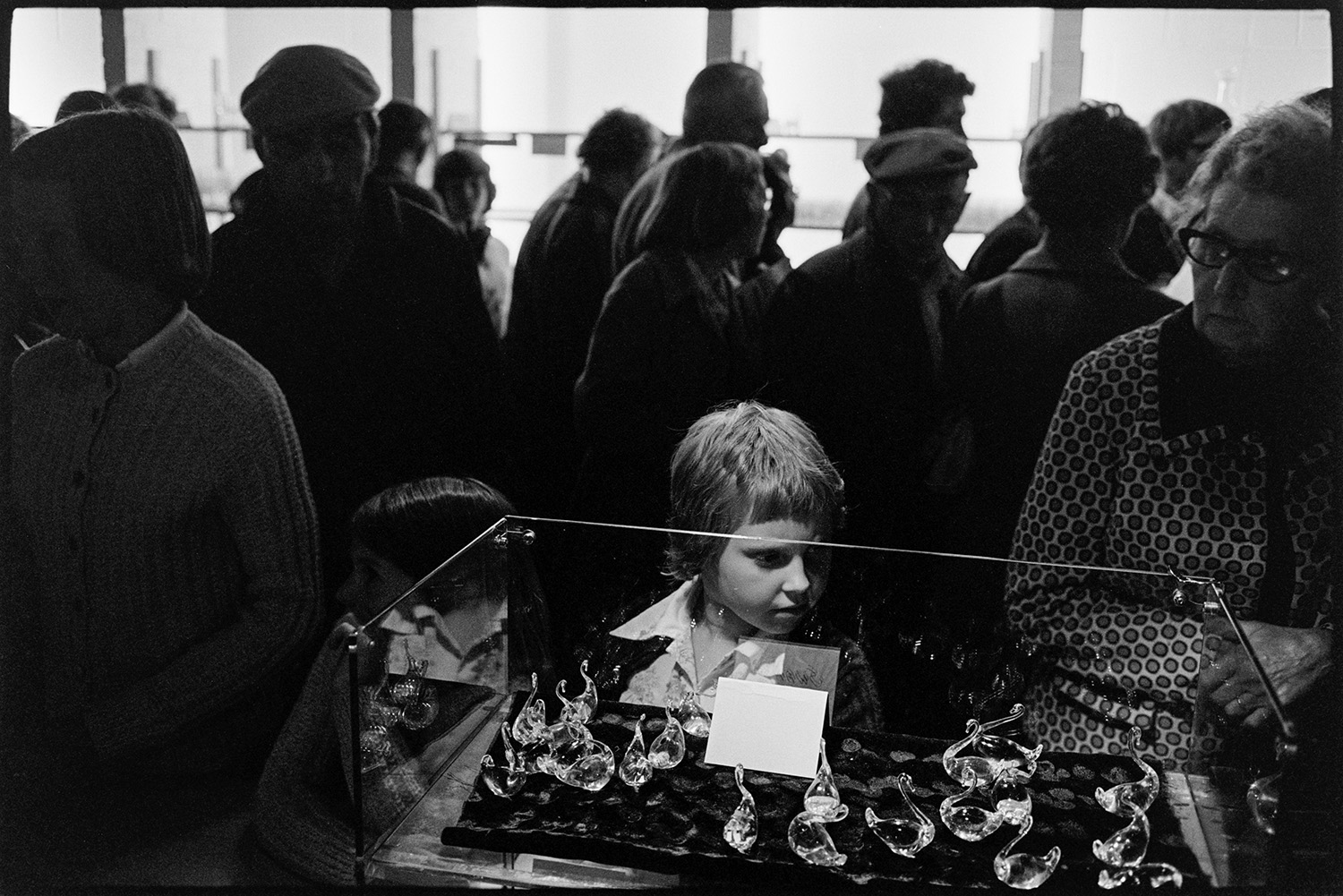 Management and workers at glass factory. 
[A boy looking at a display of glass swans for sale in the shop at the Dartington Glass factory, now known as Dartington Crystal,  in Torrington. Other customers can be seen in the background.]
