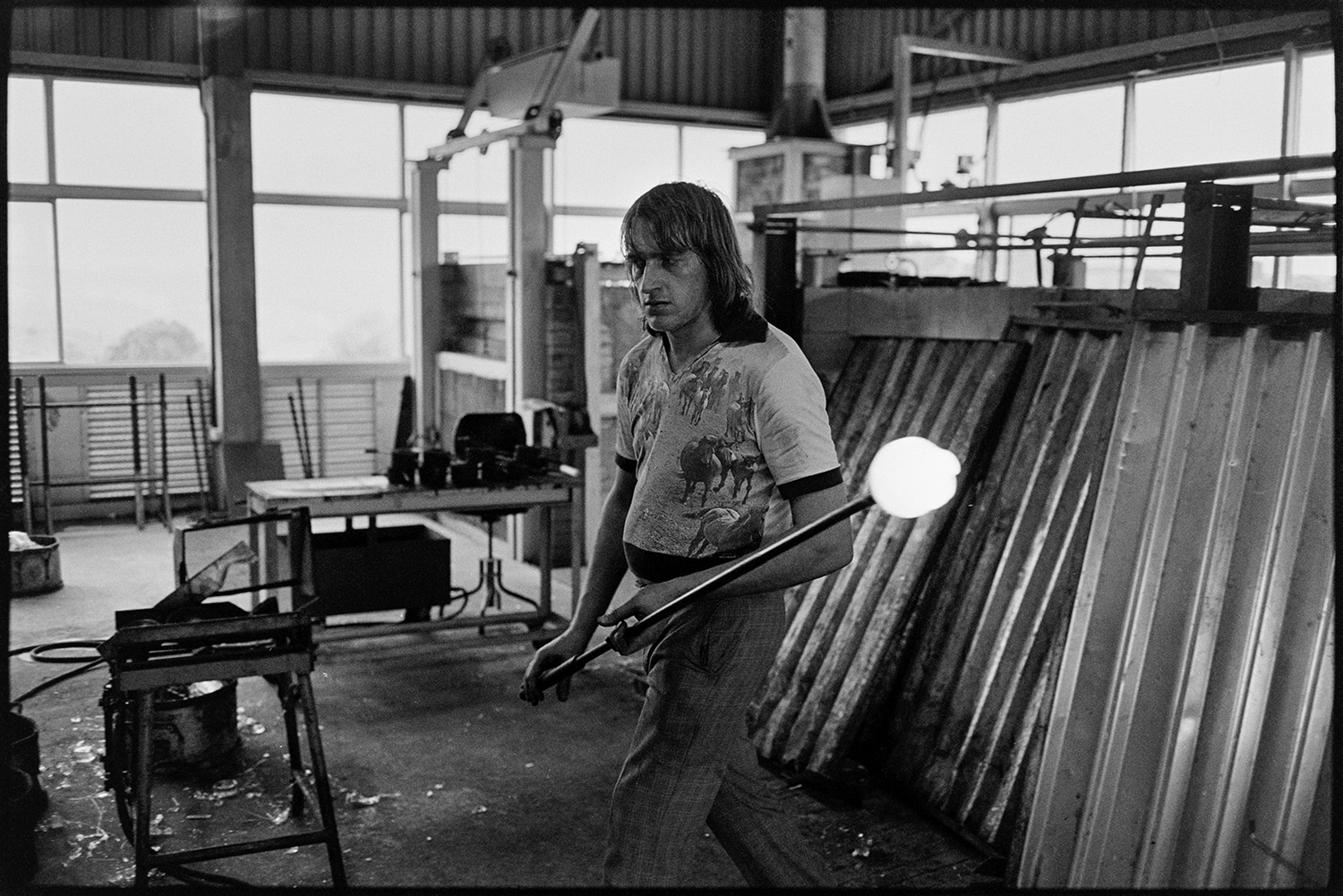 Management and workers at glass factory. 
[A man carrying a stick or blowpipe with molten glass at the Dartington Glass factory, now known as Dartington Crystal, in Torrington.]
