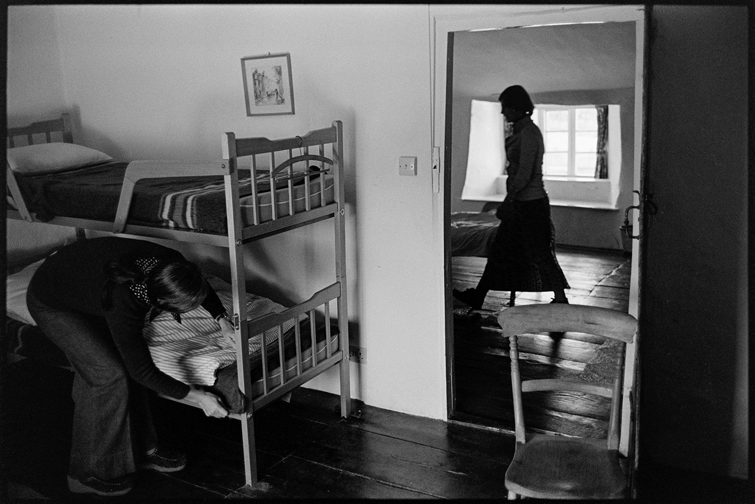 Farmhouse used as creative writing centre. 
[A person making the bottom bed of a bunk bed at the Arvon centre at Totleigh Barton, Sheepwash. A woman is walking past the open doorway to the bedroom. The farmhouse was used as a creative writing centre.]