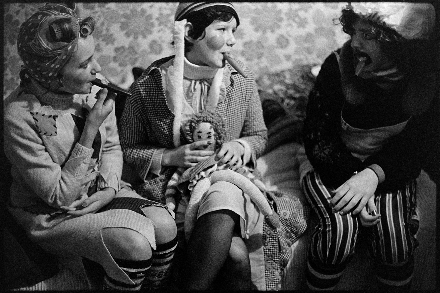 Young people in fancy dress before carnival. 
[Three young women in fancy dress before Hatherleigh Carnival. They are playing kazoos and one of them is holding a knitted doll.]