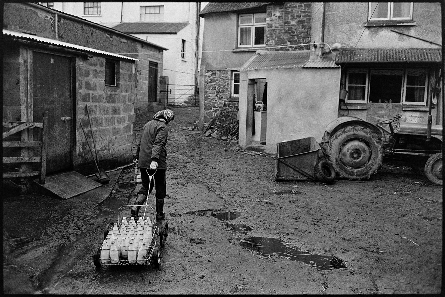 Woman delivering milk round village. <br /> [Jane Woolacott setting off from the farmyard at Verdun, Atherington to deliver milk around the village. She is pulling a trolley full of milk bottles.]