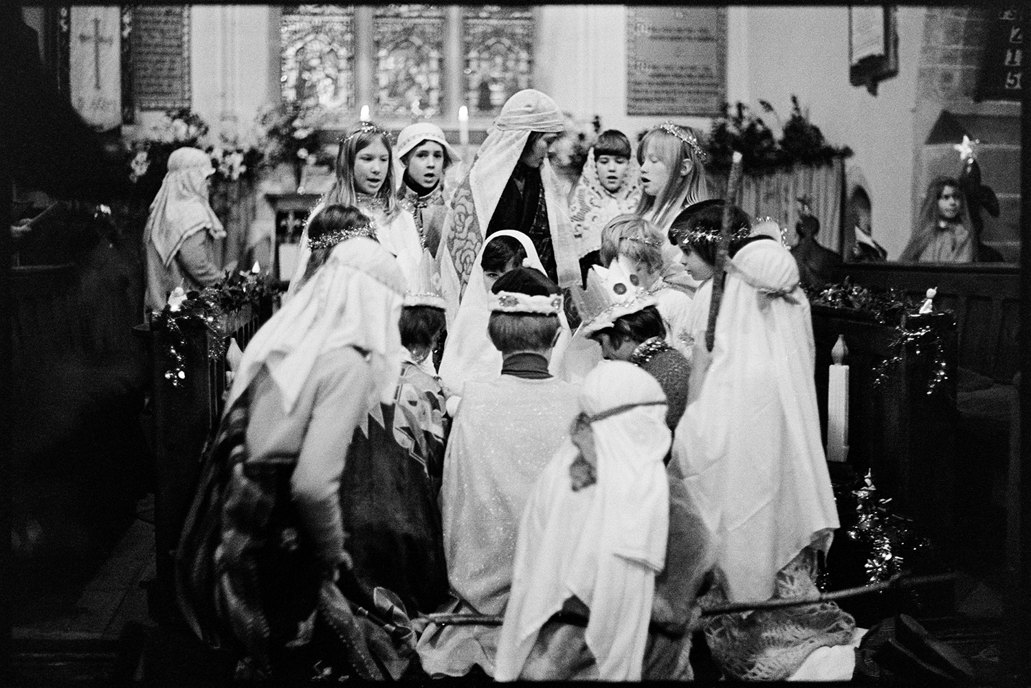 Children at Christmas Nativity play in Church. 
[Children performing in a nativity play in Dolton Church. They are dressed as angels, kings and shepherds. The pews are decorated for Christmas with tinsel.]