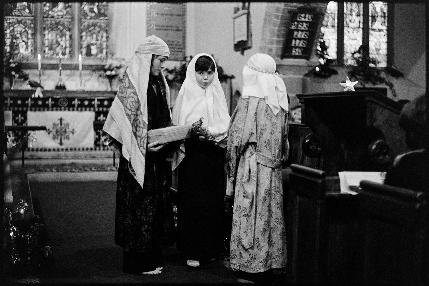 Nativity play, children in church. 
[Three children performing in a nativity play in Dolton Church. The altar can be seen in the background and the church is decorated for Christmas.]