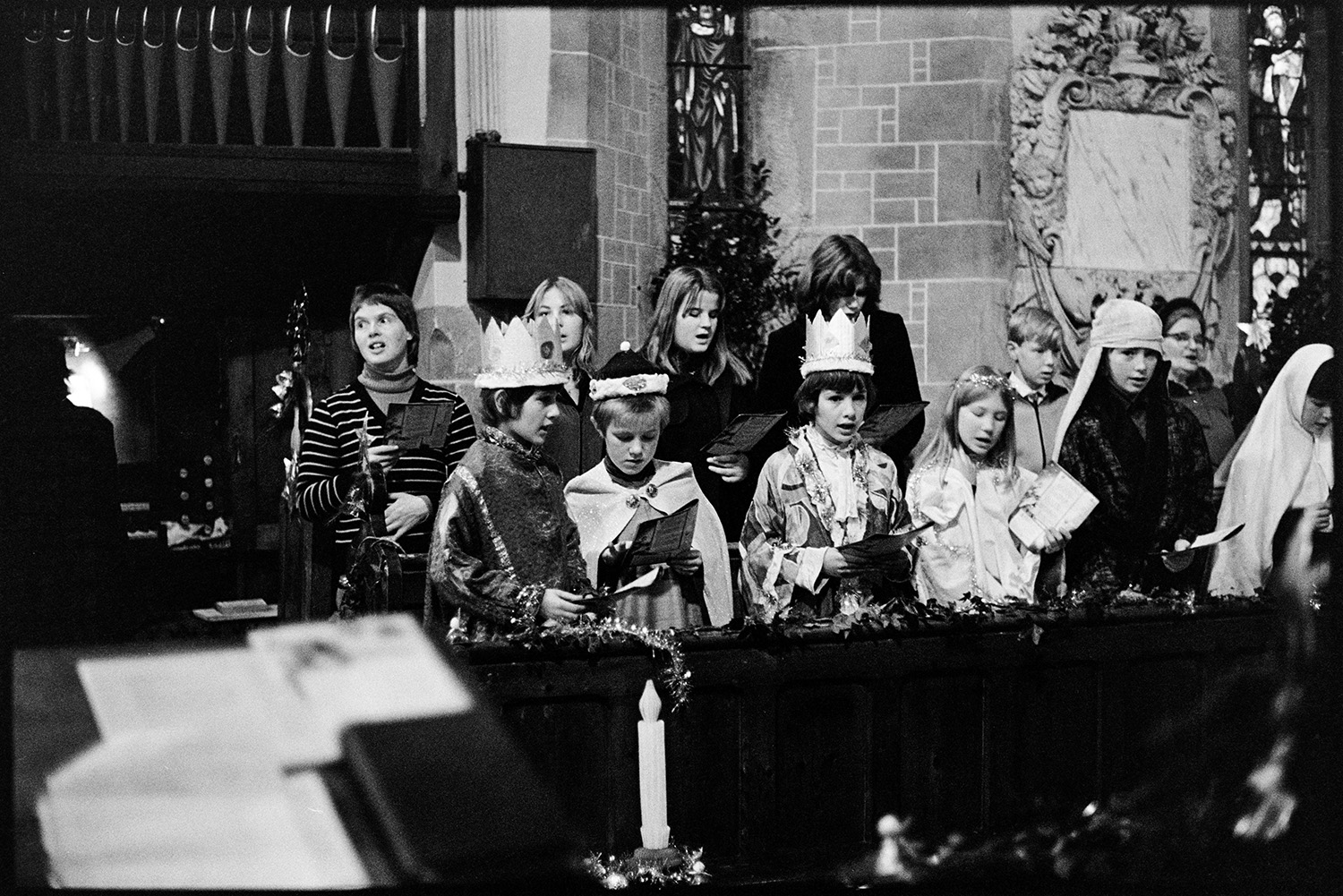Nativity play, children in church. 
[Children singing a hymn in Dolton Church. They are dressed up as kings, angels and shepherds for a nativity play. The church is decorated for Christmas with tinsel.]