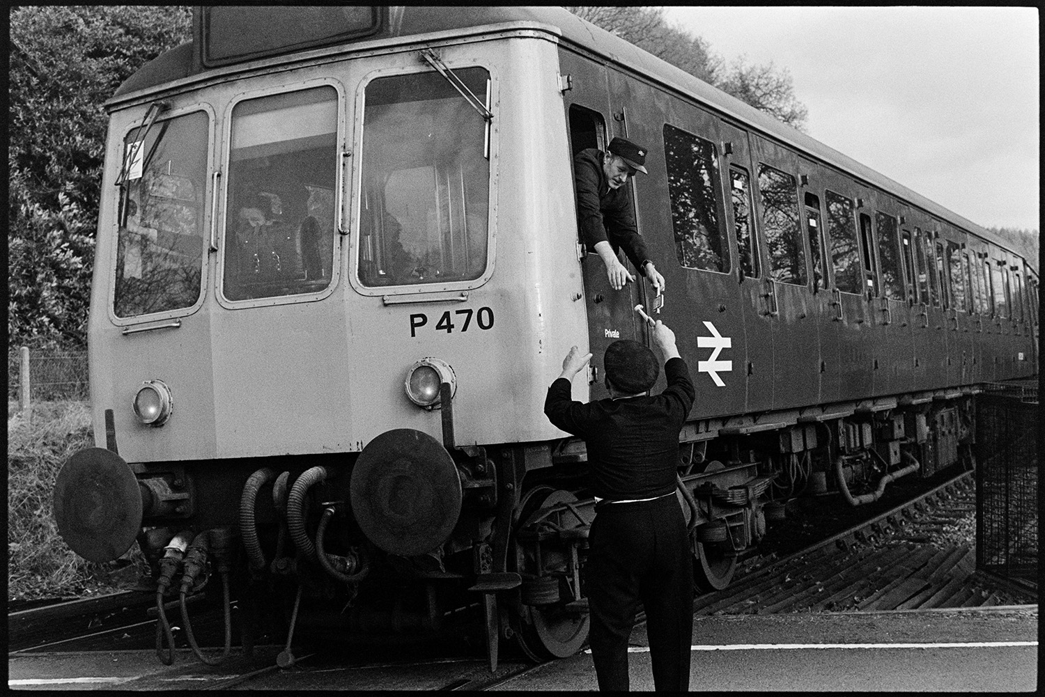 Signal box, signalman operating equipment and handing baton to train driver. 
[Jimmy Hughes handing a baton to a train driver leaning out of a train window at Eggesford Station.]