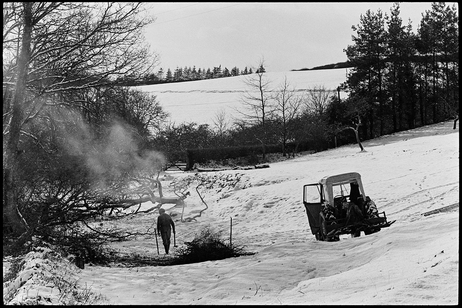 Snow scenes, farmer burning old hedge cuttings. 
[A man burning hedge cuttings in a snow covered field at Westpark, Iddesleigh. A tractor is parked in the field and the man is holding an axe.]