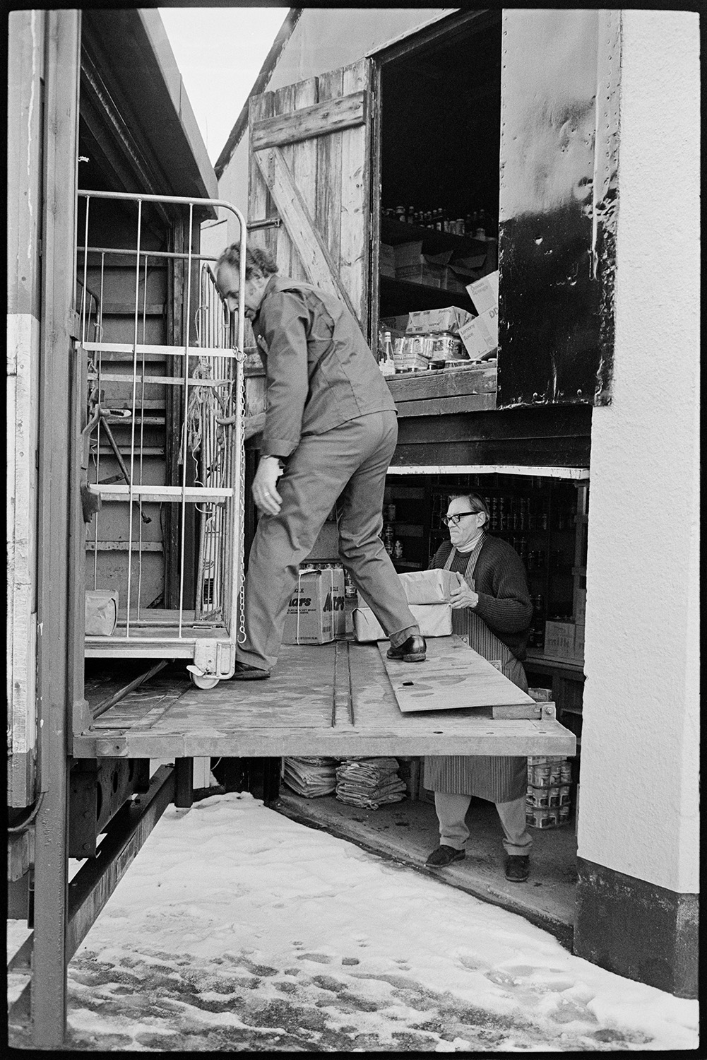 Man unloading groceries from back of lorry. 
[Two men unloading groceries from a lorry and loading them into a store or warehouse in Church Street, Dolton.]