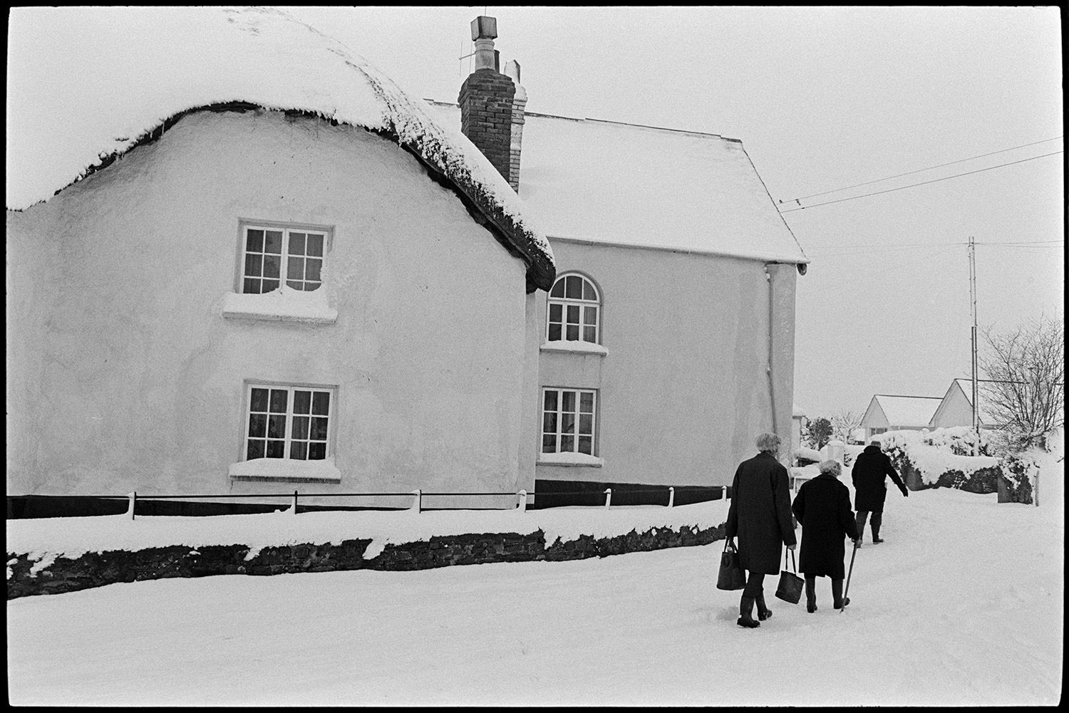 Snow, street scenes, postman handing out mail, shoppers, etc. Tractor and link box. 
[Men and women walking along a street in Dolton in the snow. They are passing a thatched cottage covered in snow.]