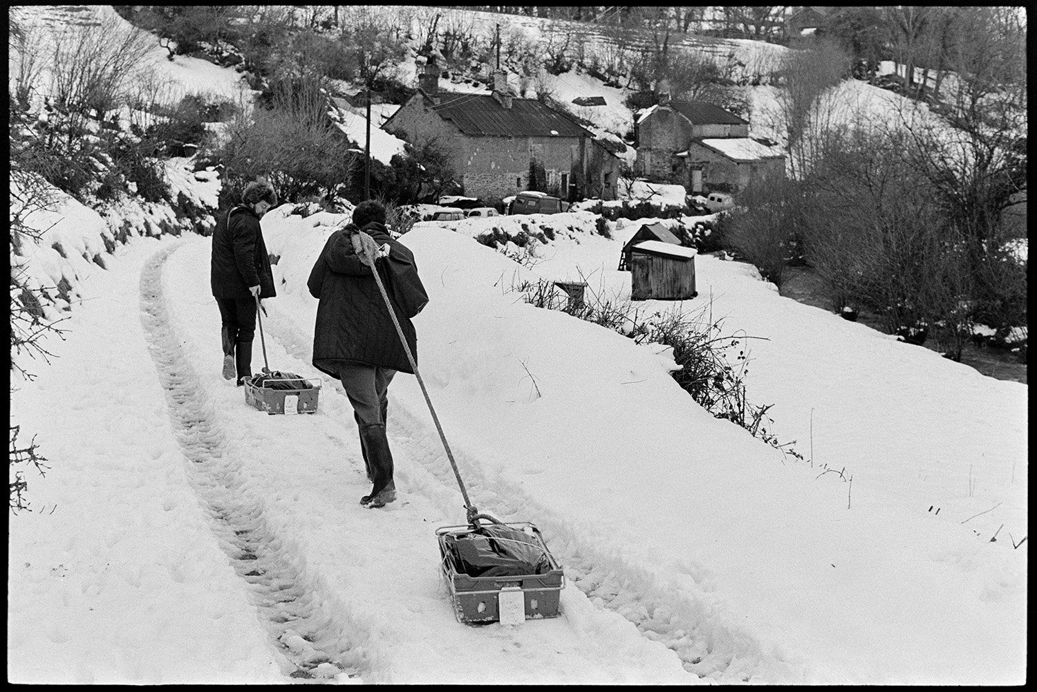 Snow, butcher setting off with meat on sledge for next village, Merton cut off. 
[Bill Davey, butcher, and another person dragging sledges with meat along a snow covered lane at Millhams, Dolton. They are going to deliver the meat to Merton which was cut off in the snow.]