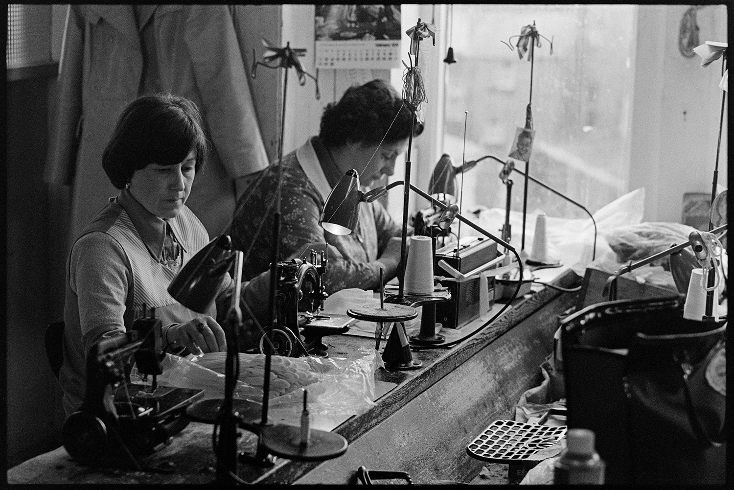 Glove factory. Women at factory machines. Woman clerk filling in ledger.
[Two women seated at sewing machines making gloves at Vaughans Glove Factory, Halsdon Terrace, Torrington.]
