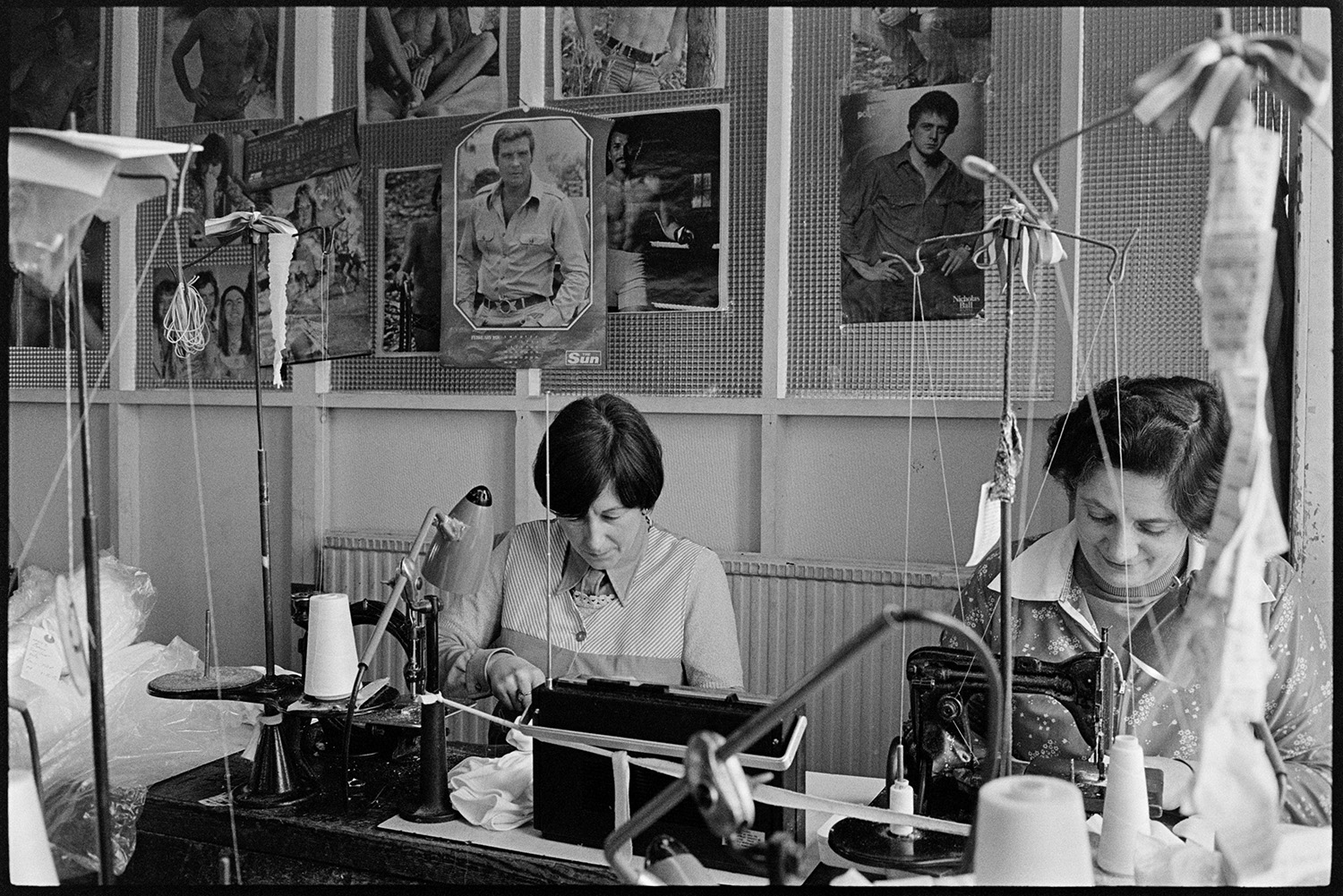 Workers in glove factory. Machinery. Pin-ups!
[Women working at sewing machines at Vaughans Glove Factory, Halsdon Terrace, Torrington with posters on the wall behind them.]
