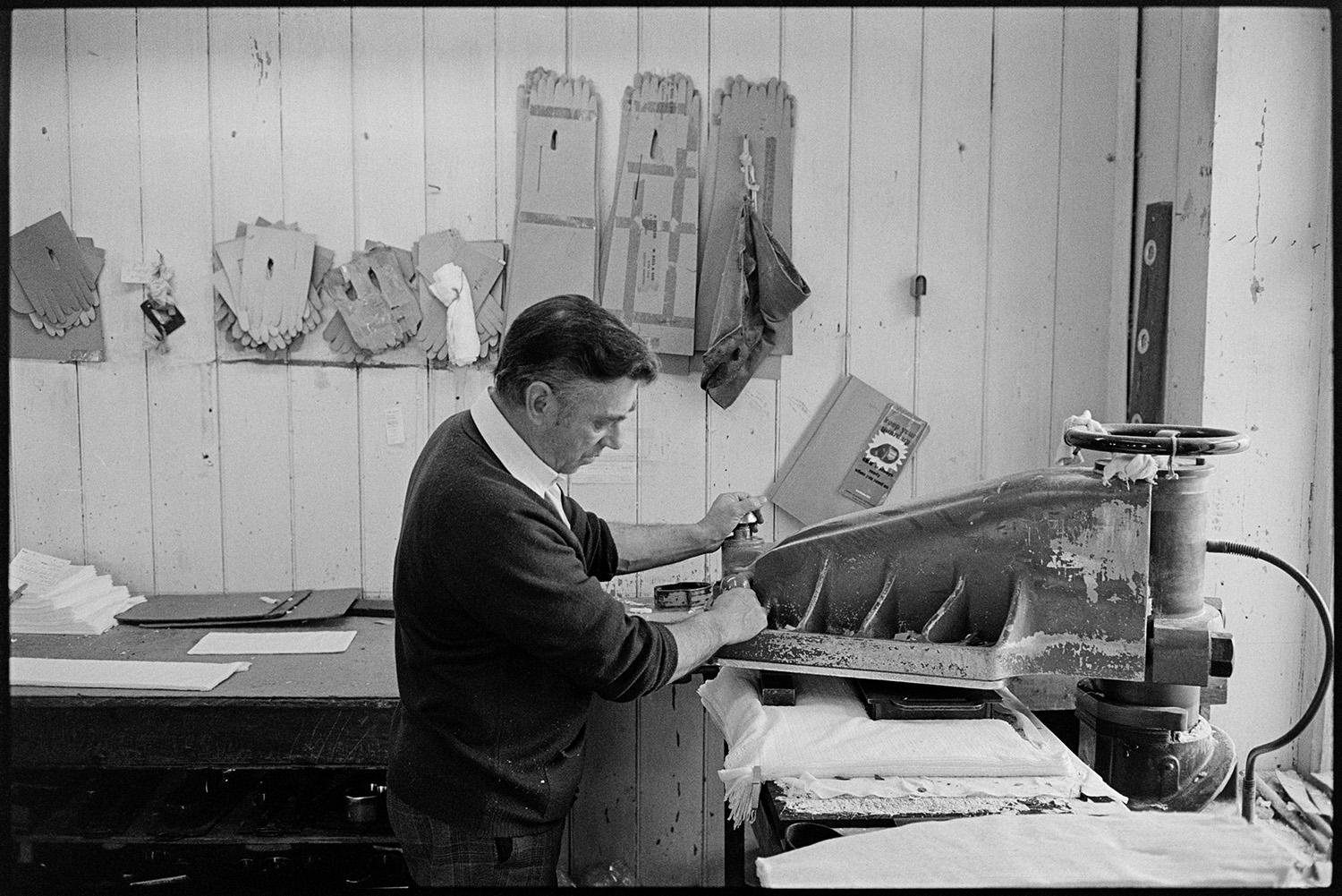 Workers in glove factory. Machinery. Pin-ups!
[A man working with machinery at Vaughans Glove Factory, Halsdon Terrace, Torrington. Glove templates are hung on the wall behind him.]