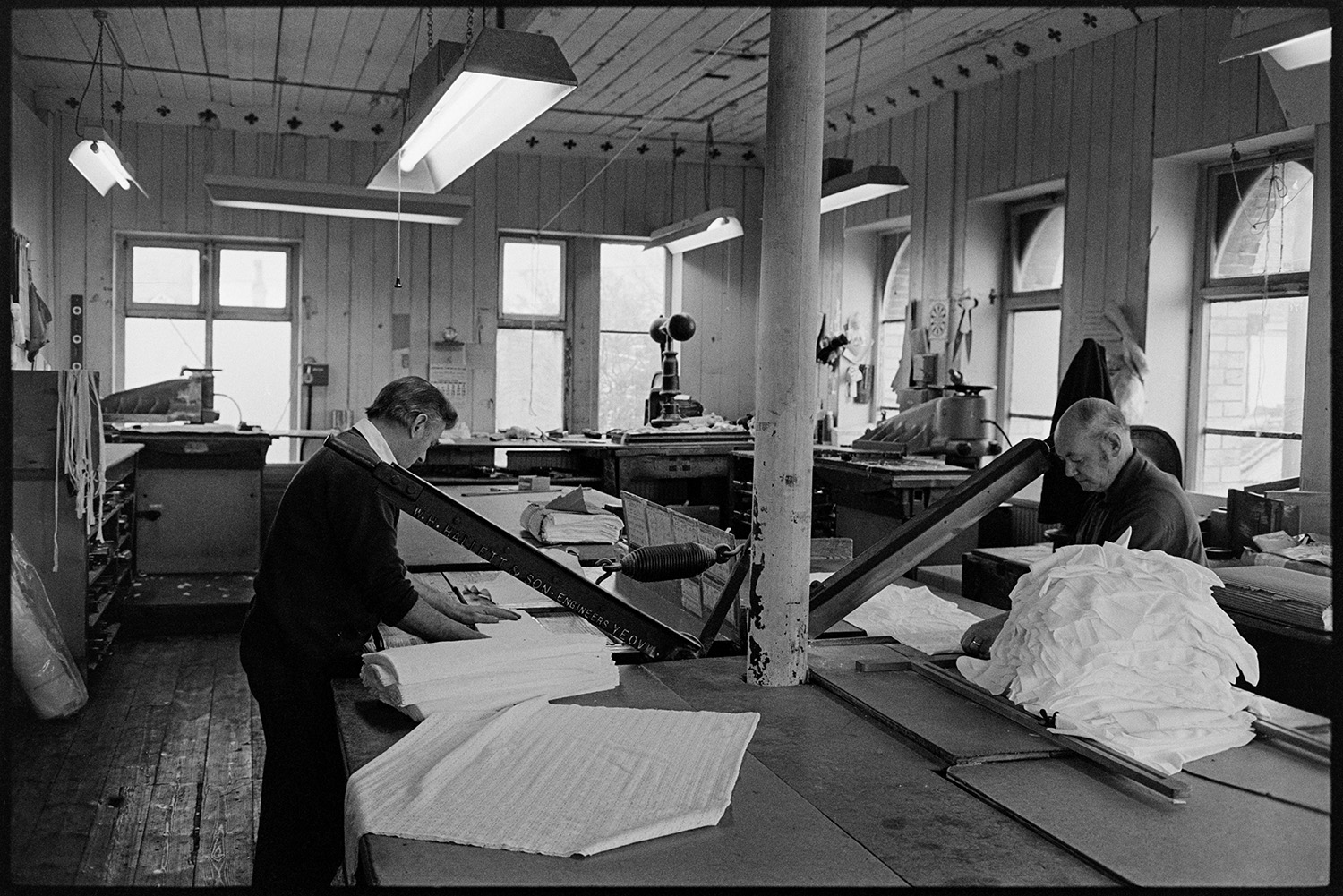 Workers in glove factory. Machinery. Pin-ups!
[Men working with machinery at Vaughans Glove Factory, Halsdon Terrace, Torrington. They are cutting pieces of fabric with large guillotines.]