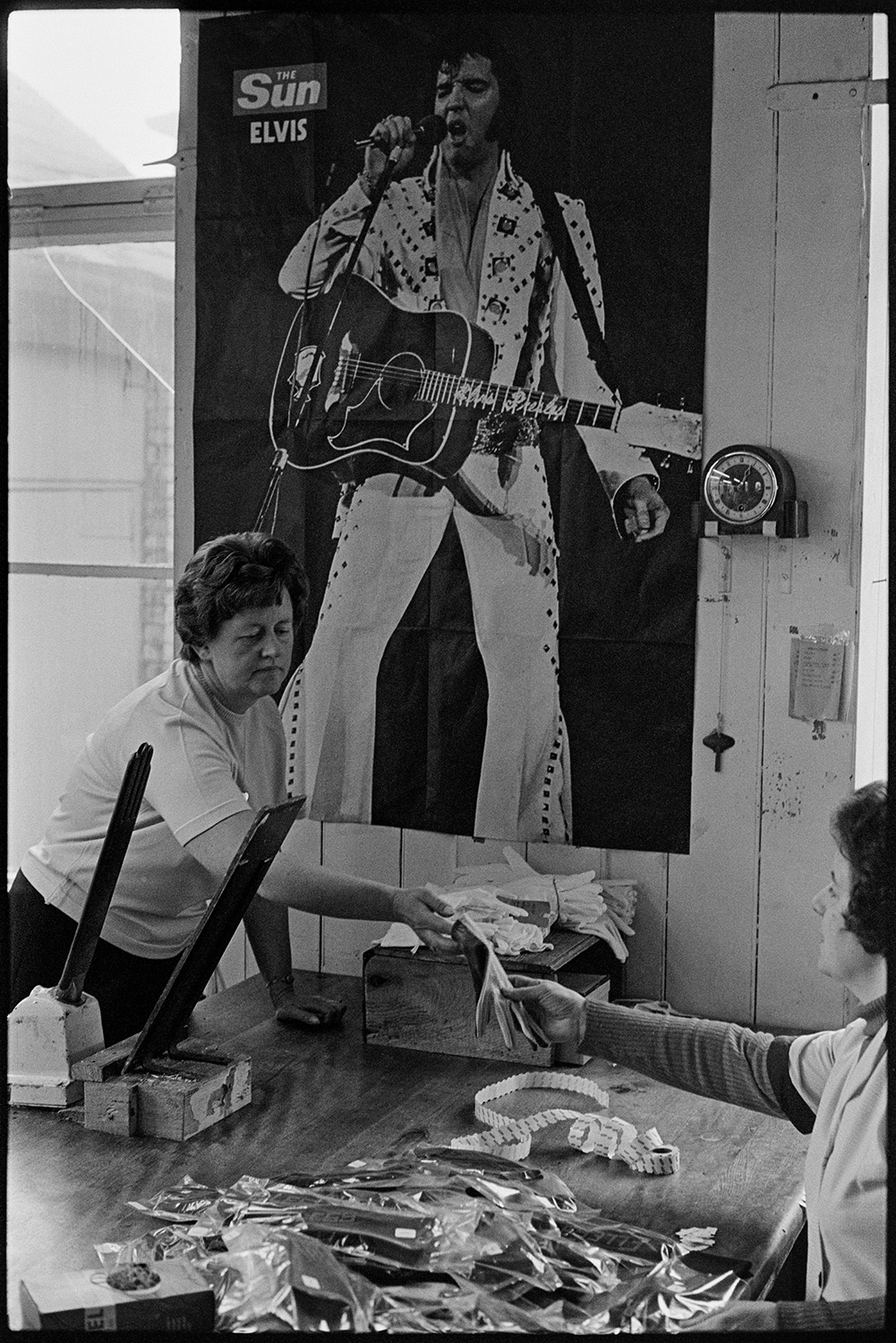 Workers in glove factory. Machinery. Pin-ups!
[Women working at Vaughans Glove Factory, Halsdon Terrace, Torrington by a big poster of Elvis on the wall.]