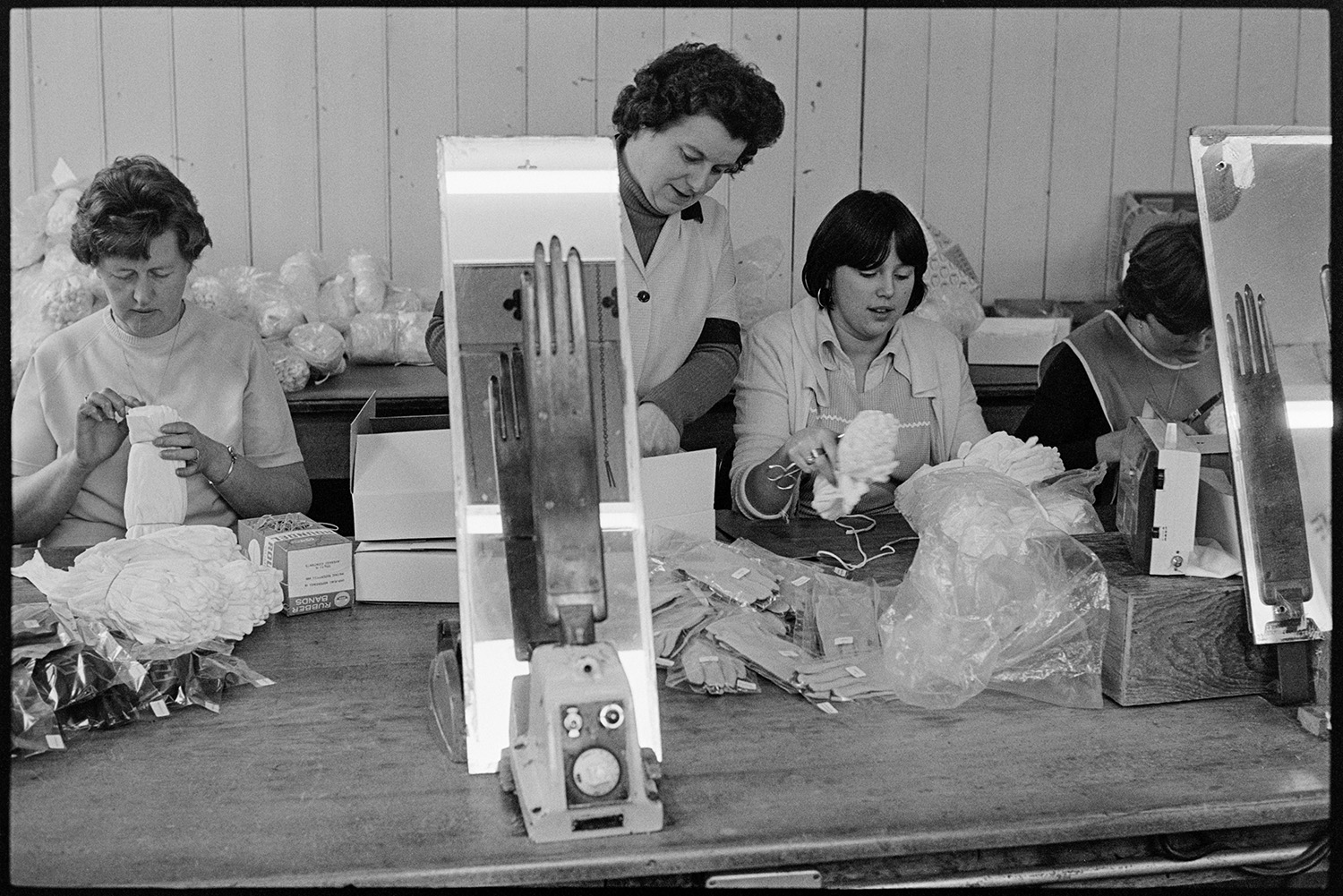 Workers in glove factory. Old machinery. Canteen. Office with man on telephone. Deliveries.
[Women working at Vaughans Glove Factory, Halsdon Terrace, Torrington. They are checking and bagging up the gloves.]