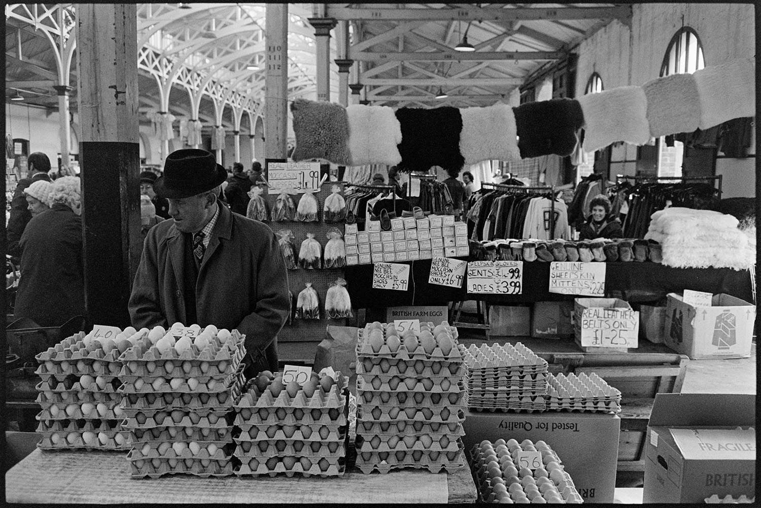 Stalls at Pannier market. Eggs, vegetables, flowers.
[A man selling eggs at a stall in Barnstaple Pannier Market. A stall selling hats, sheepskin gloves and moccasin slippers is visible in the background.]