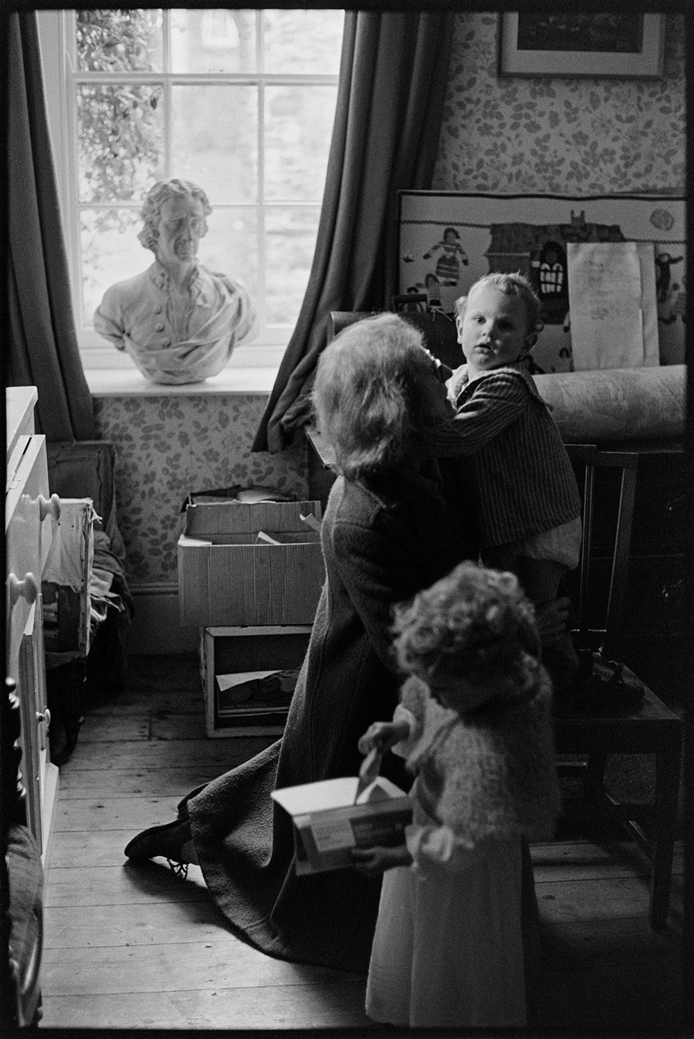 Christening. Family at home and outside Church with vicar.
[A woman with a baby and young child in a room at Clovelly after a christening in the Rous family. A bust of a man is displayed in the window.]