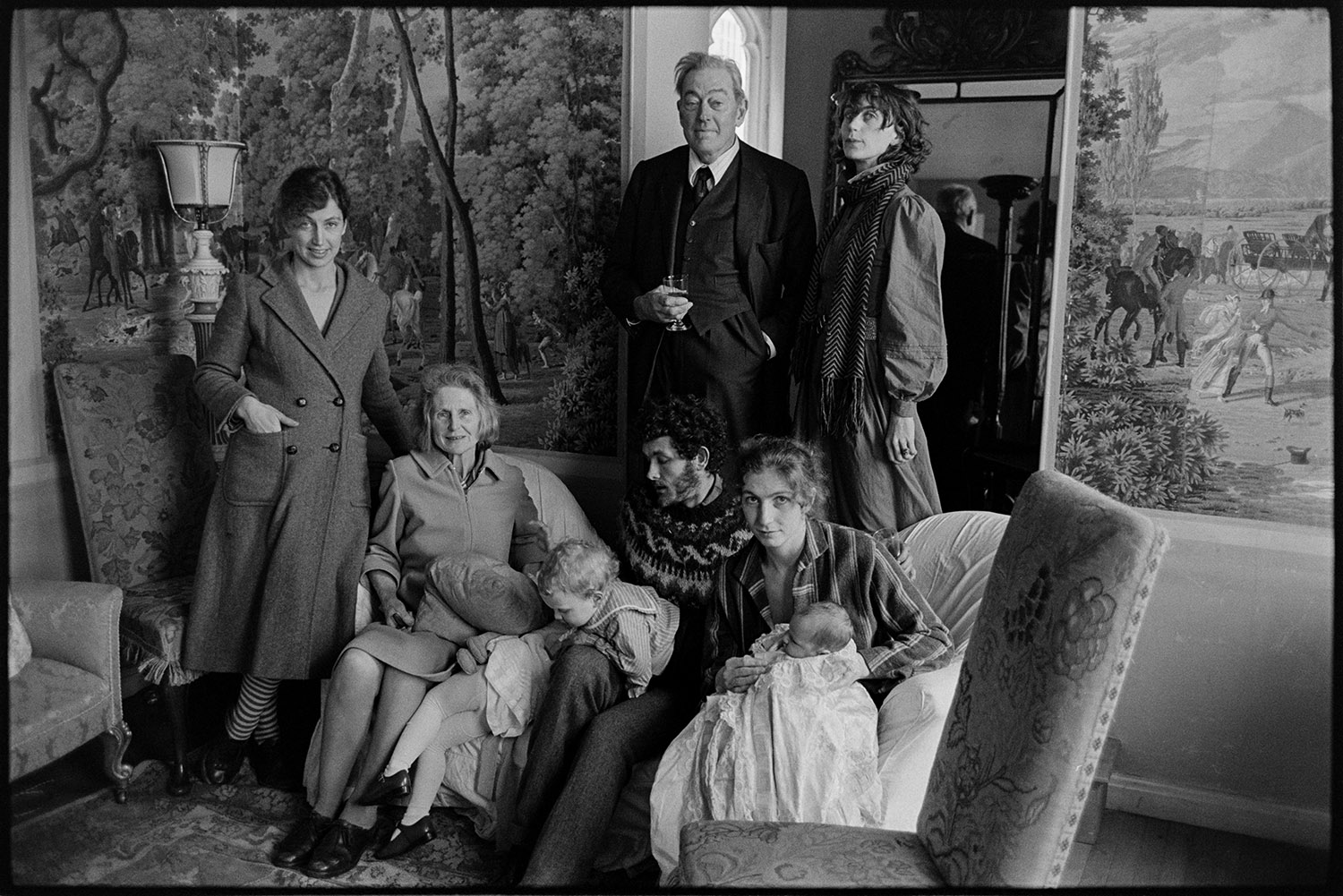 Christening, family groups at home after service, family taking photographs. <br />
[Several generations of the Rous family posing for a photograph in a room at Clovelly Court, after a christening. A woman sat on a chair is holding the child which has been christened. Tapestries are hanging on the walls.]