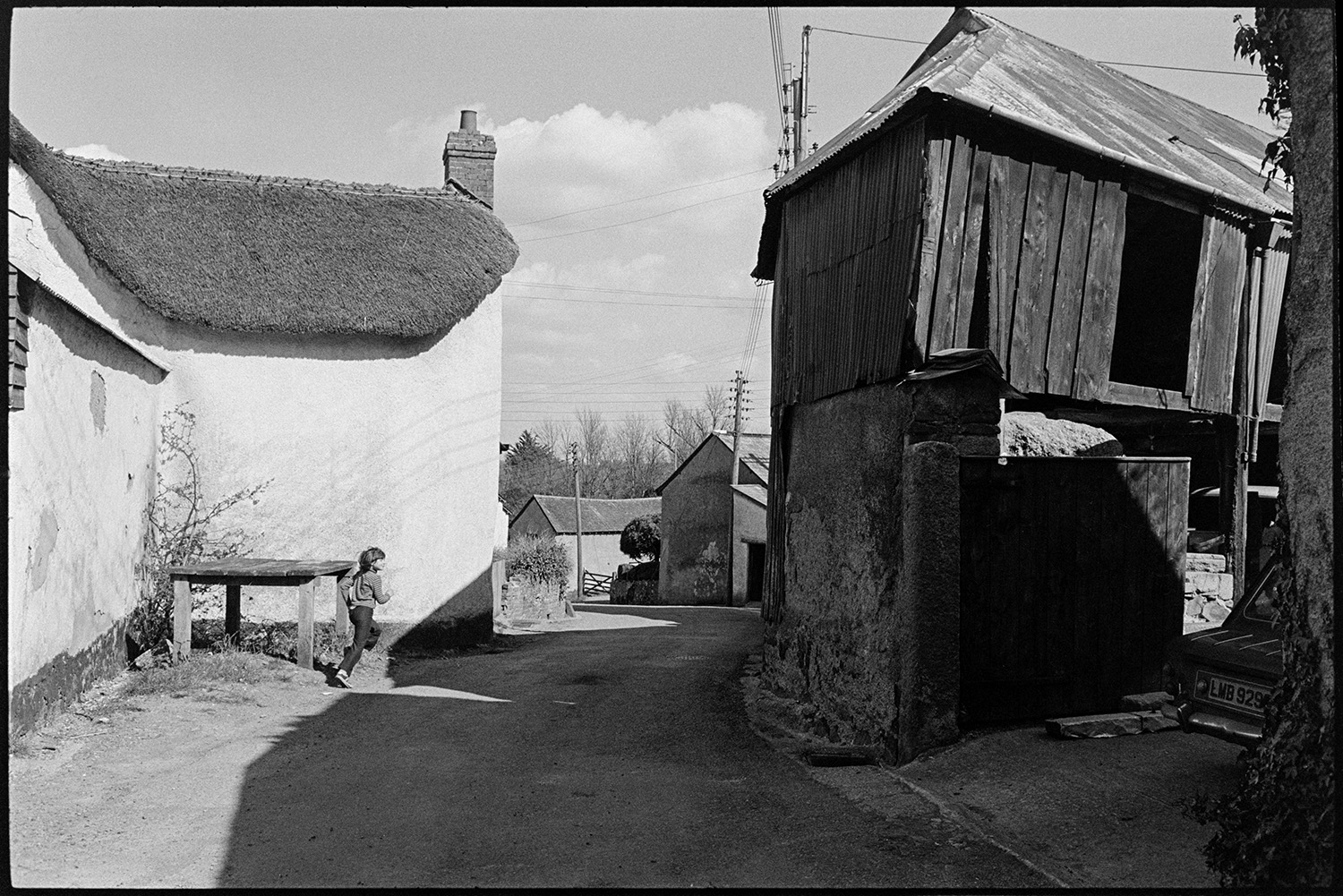 Street scenes with horse and Georgian house, wooden barn. 
[A child running past a wooden milk churn stand by a thatched cottage in Exbourne. A wooden barn is on the opposite side of the street.]