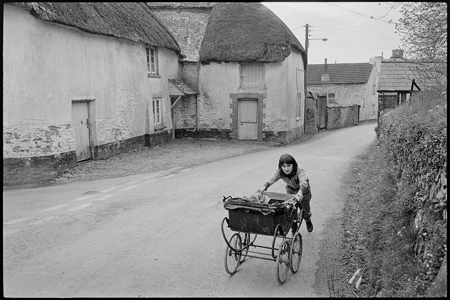 Baker selling from van, horse and children with pram. 
[A child pushing an old fashioned pram along a street in Roborough, past a thatched farmhouse, opposite the church.]