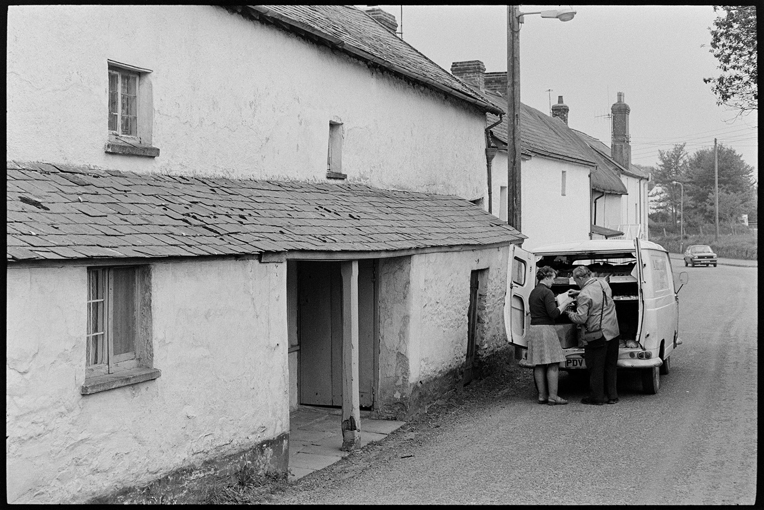 Bakers van in front of house with interesting doorway, now enlarged and ruined as usual!!! 
[A woman buying goods from a baker's van parked in front of cottages with a long porch at Rectory Road, Dolton. The cottages were later renovated.]