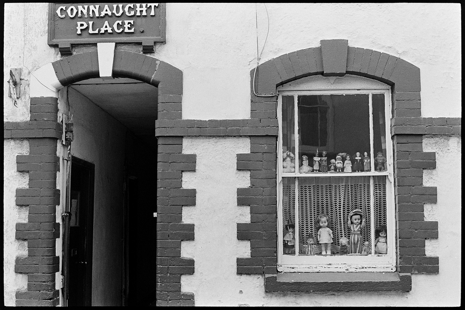 Window with dolls. 
[A display of dolls in a window at Connaught Place on Silver Street, Barnstaple.]