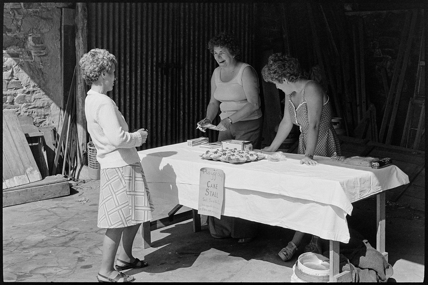 Women at cake stall in aid of children's playgroup. 
[A woman buying cakes from Pam Stiles (on the left) and another women running a cake stall to raise money for the children's playgroup in Dolton. They are talking and laughing.]