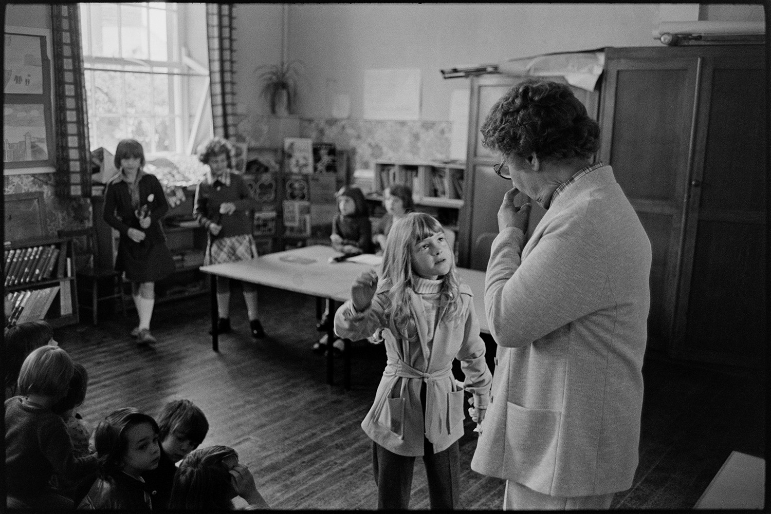 The Headmistress talking to a girl in an assembly at Blue Coats School, Torrington. Recorder players can be seen in the background.]