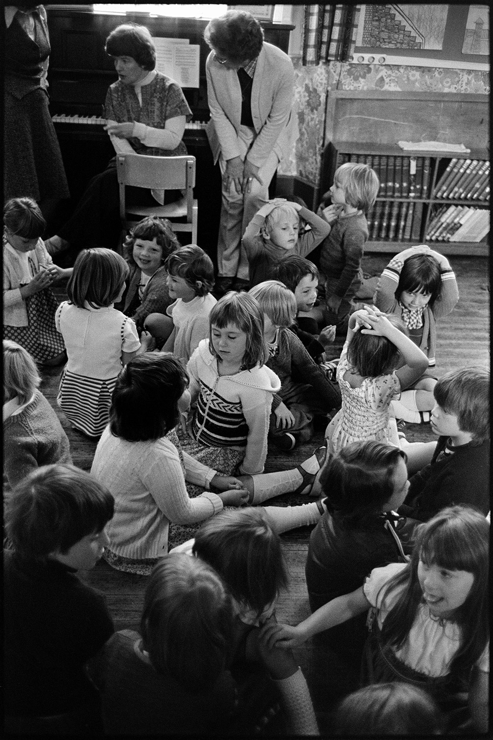 Children talking and laughing in an assembly at Blue Coats School, Torrington. Some of the children have their hands on their heads. Teachers can be seen in the background.