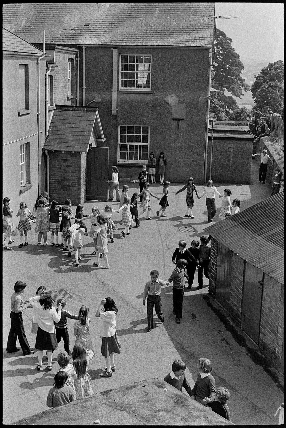 Children playing in school playground, holding hands in circle. 
[Children playing in the playground at Blue Coast School, Torrington. They are holding hands and running around.]