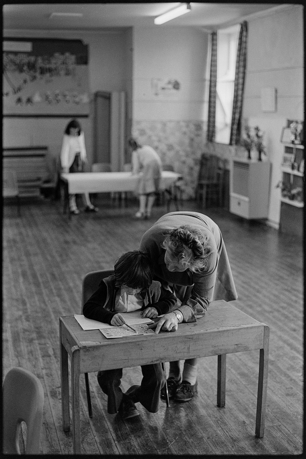 Schoolchildren and teachers in class, reading and asking questions. 
[A teacher helping a child with school work at a desk in a classroom at Blue Coats School in Torrington.]