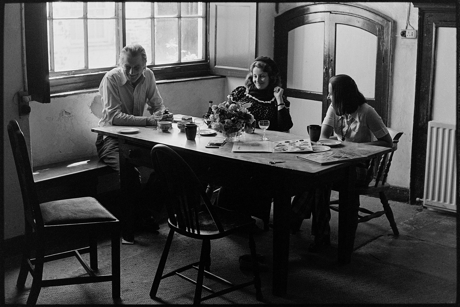 People sitting round kitchen table of large country house. 
[Robin Ravilious, Pat Furse and Antonia Furse sat around a kitchen table and talking at Halsdon House in Dolton.]