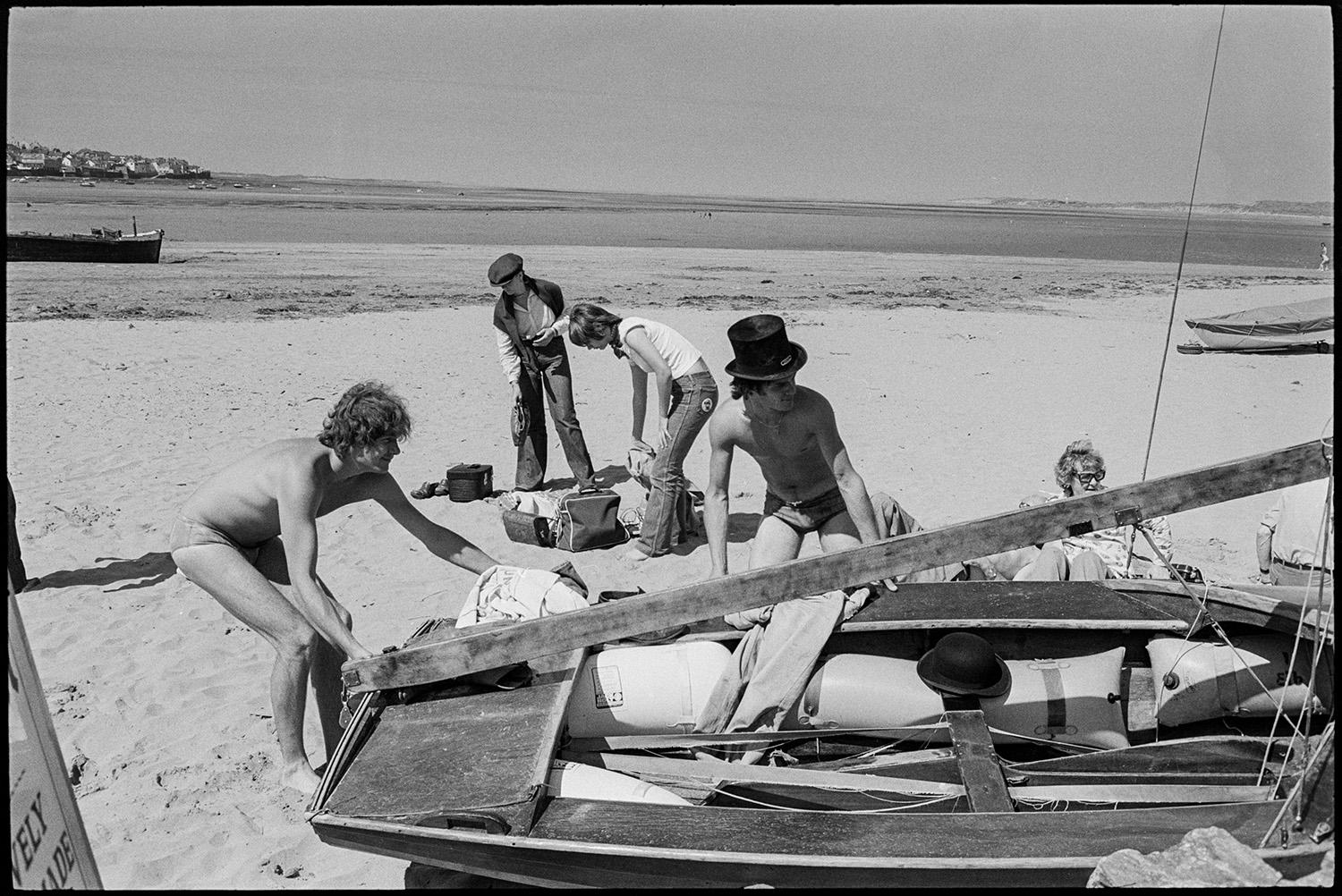 Holidaymakers, sailing boat. 
[Men moving a small boat on Instow beach. One of the men is wearing a top hat. A woman and other holidaymakers can be seen in the background.]