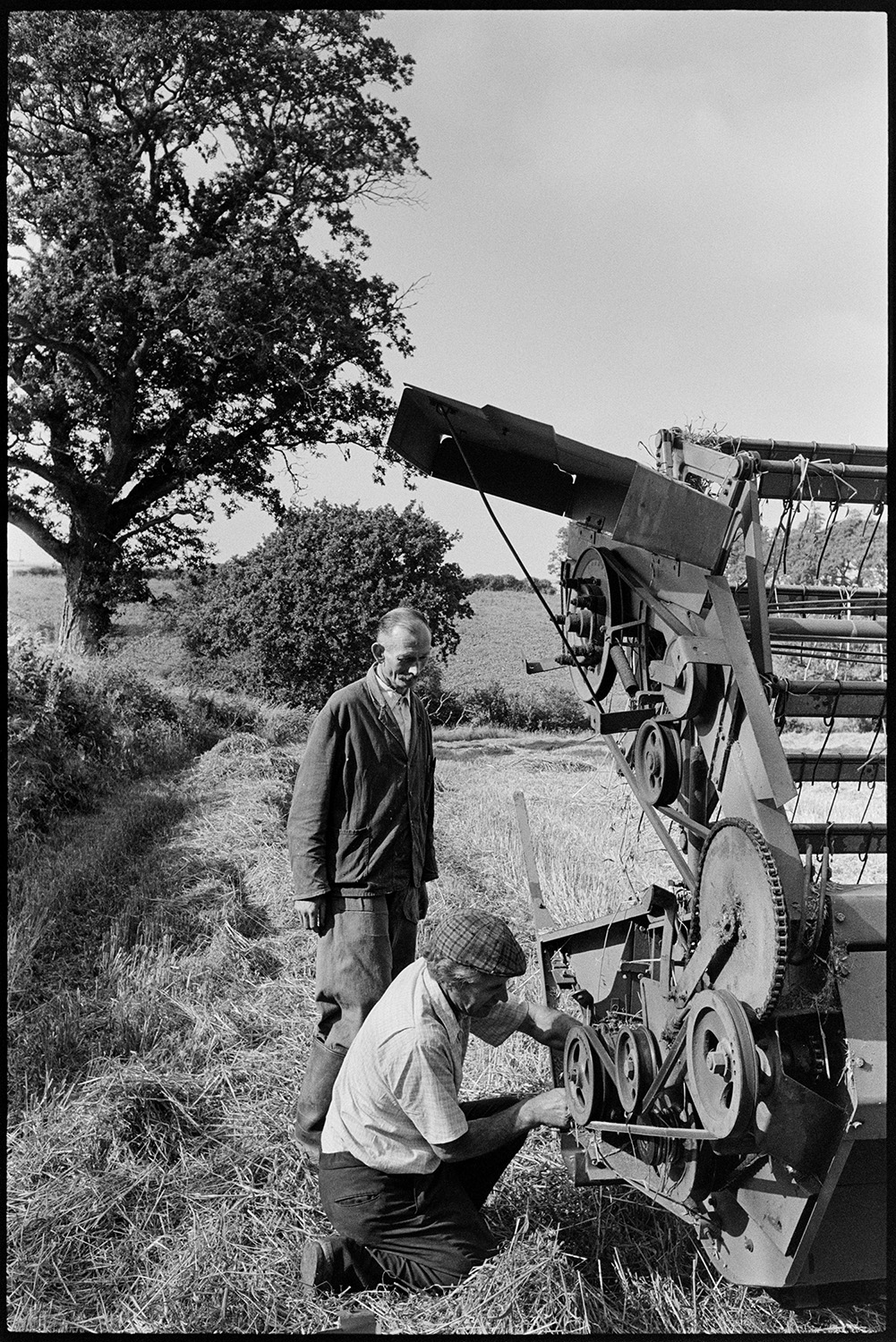Combine harvester maintenance. 
[Mr Dunn and another man checking the mechanics of a combine harvester in a field at Dowland.]