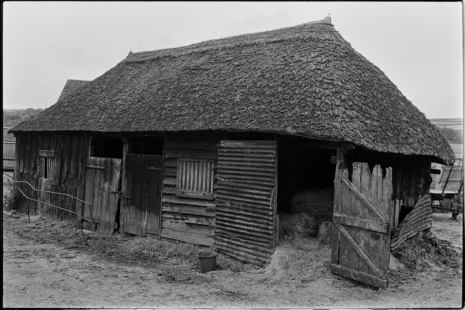 Wooden barn with thatched roof now demolished. 
[A wooden barn with a thatched roof at Leigh Farm, Chulmleigh. Hay bales can be seen through the open door of the barn.]